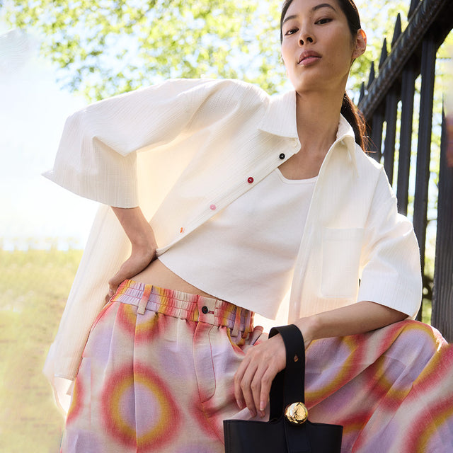 wOMAN WEARING OVERSIZED WHITE BUTTON-UP SHIRT AND ORANGE GROOVY PRINT WIDE LEG TROUSERS BOTH BY CHRISTOPHER JOHN ROGERS 