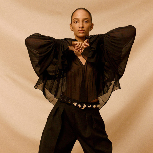 Woman wearing black sheer blous, black pants and black and silver studded belt by Khaite