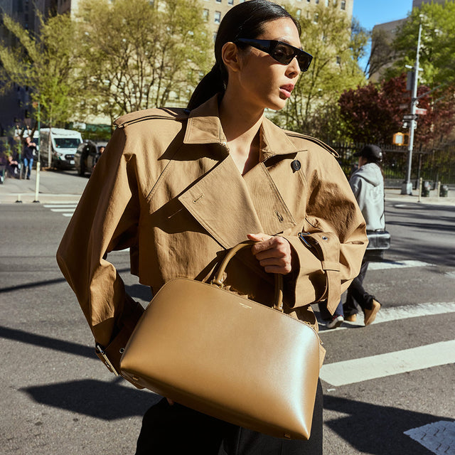 Woman wearing brown cropped trench jacket by Khaite carrying Sac Du Jour duffle bag by Saint Laurent 