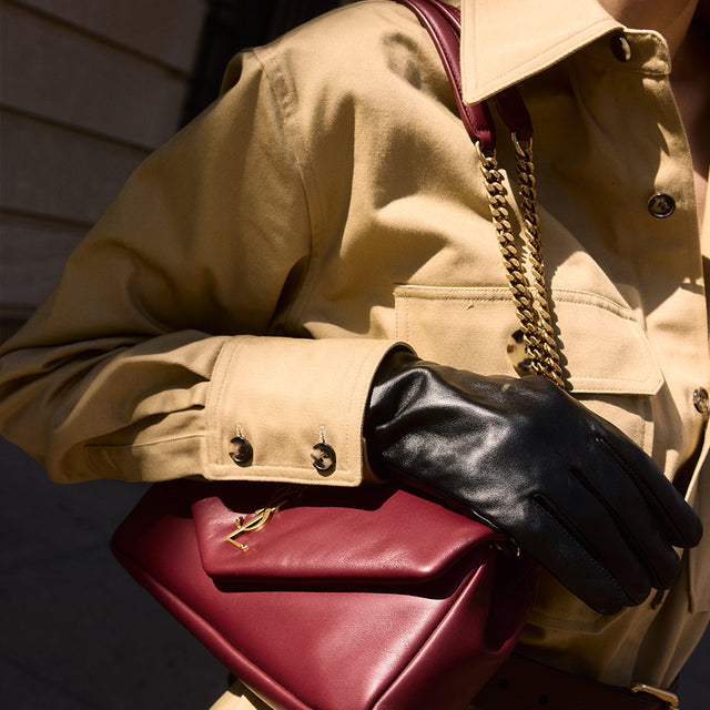 Woman wearing khaki twill jumpsuit carrying burgundy leather Calypso shoulder bag with chain strap, both by Saint Laurent  