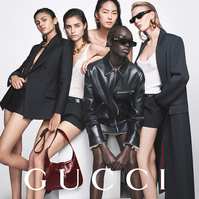 5 female Models wearing black and white apparel carrying a burgundy patent hobo bag, all by Gucci  