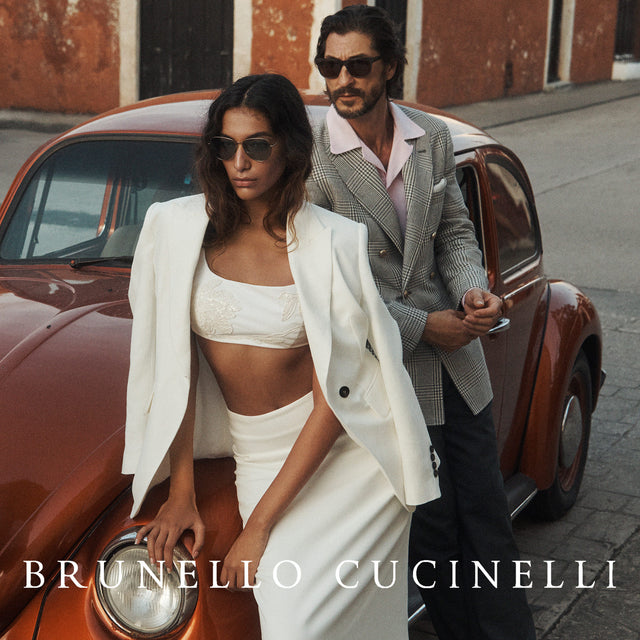 Woman wearing white bra-top, jacket and skirt and man wearing black sportscoat and pink shirt, all by Brunello Cucinelli 