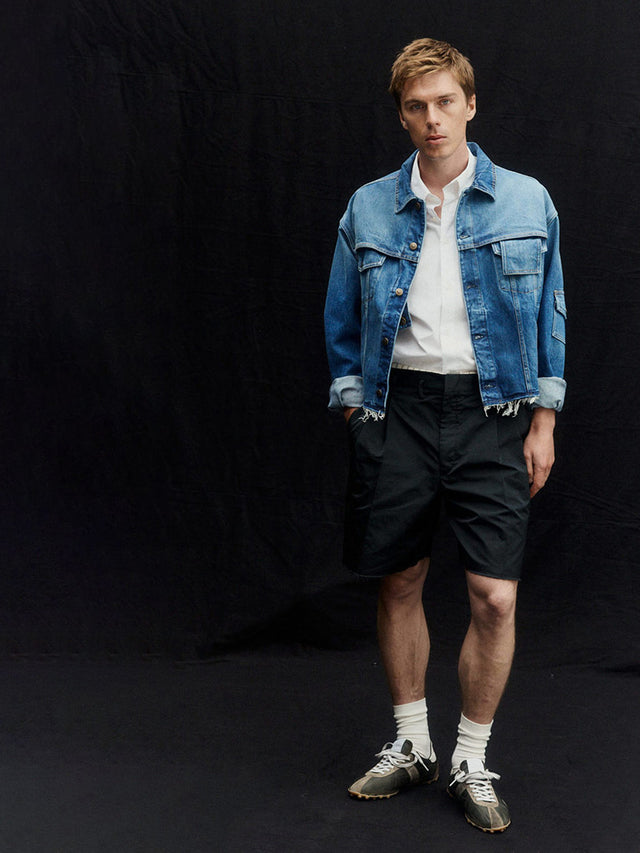 Man wearing Maison Margiela denim jacket, white shirt, black shorts, and sprinter sneakers on a black background