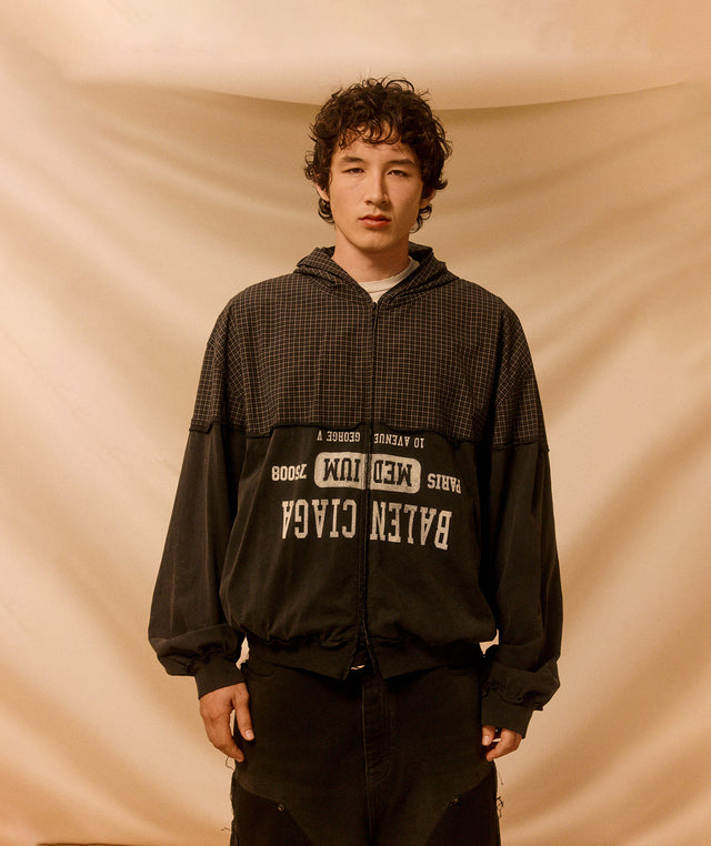 Person wearing a black hooded Balenciaga jacket with brand logos against a beige background