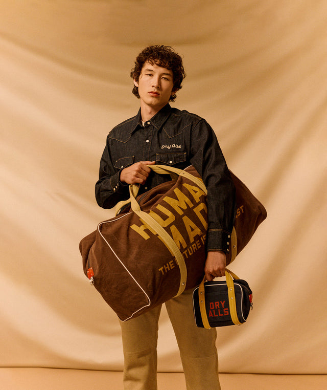 Person holding a brown HUman Made duffel bag and smaller Fry Alls dopp kit