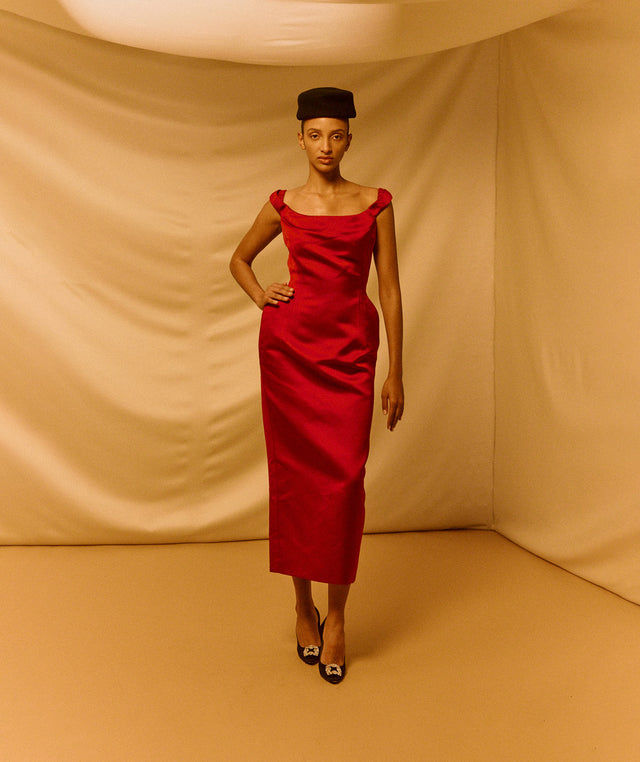 Woman in a red dress by Magda Butrym and black hat standing against a beige background