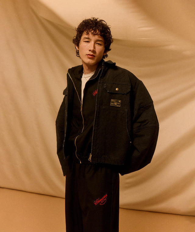 Person wearing a black Willy Chavarria jacket and pants with red accents against a beige background