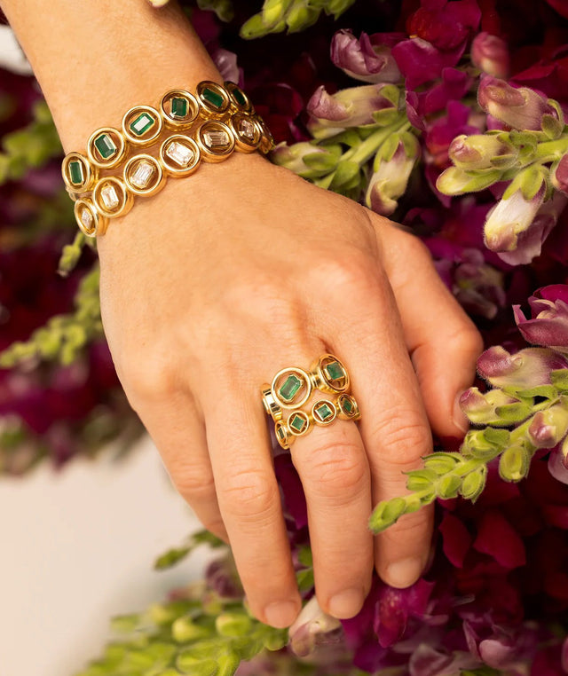 Hand wearing 2 gold and emerald rings, a gold and emerald bracelet and gold and diamond bracelet by Jenna Blake  