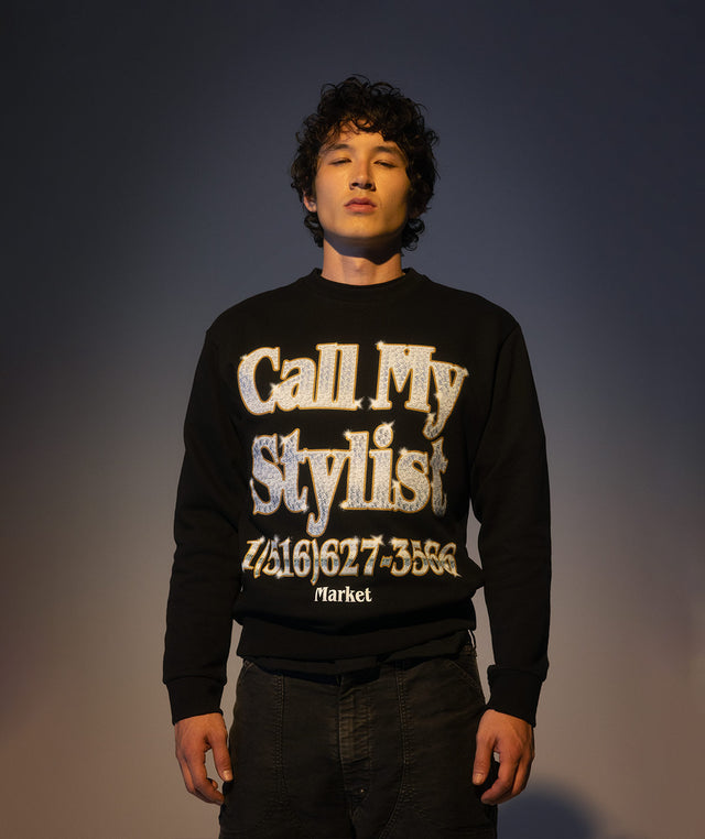 Person wearing a black sweater with 'Call My Stylist' text from the Market x Hirshleifers collection