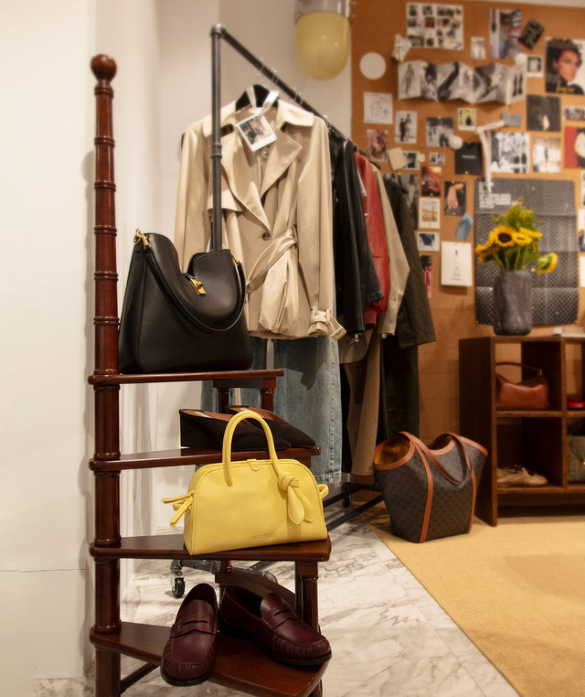 Hirshleifers store #OurEdit section- clothing rack with bags and shoes in a room with a bulletin board and shelving.