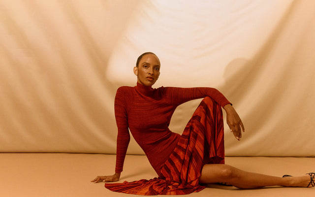 Woman in a red dress by Christopher John Rogers posing against a beige background