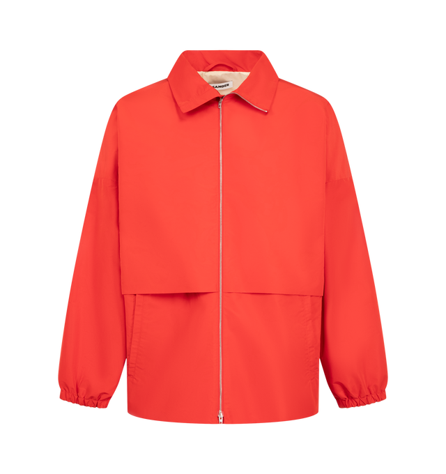 Image 1 of 3 - RED - Jil Sander Men's Technical Faille Blouson is crafted from technical faille and features a relaxed-fit silhouette with dropped shoulders, a stand collar, and a pack-away hood concealed within the collar. Designed for versatile everyday wear, this lightweight jacket is finished with a front zip closure, side welt pockets, a drawstring waist, elasticized cuffs, and a signature Jil Sander logo application at the sleeve. Main Material: 100% Polyester. Fit: Relaxed. Collar: Stand Collar with