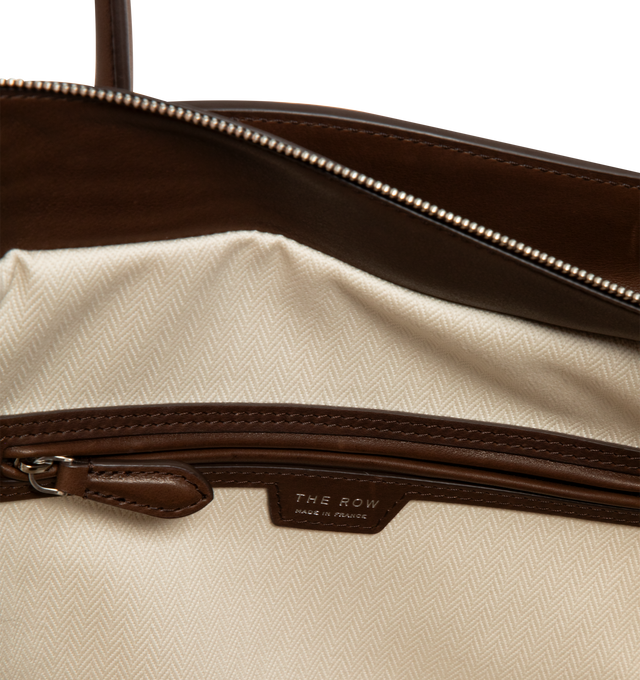Image 3 of 3 - BROWN - The Row Marlo 14 softly structured tote bag in polished saddle leather with tubular handles, gusseted side panels, and top zipper closure. 100% calfskin leather; 100% cotton lining. Made in Italy. Measures 14 x 6.2 x 10.5".