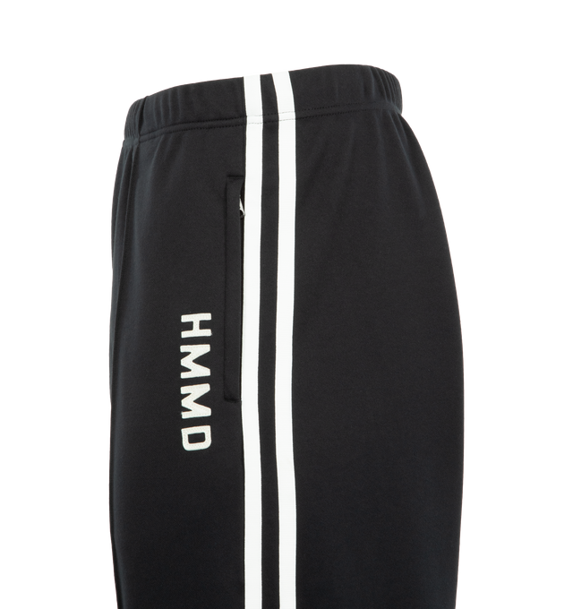 Image 4 of 4 - BLACK - HUMAN MADE Track Pants featuring straight cut with sharp front pleats, stripes down side seams, elasticated waist, two front pockets, one back pocket, vented hem and text graphic on leg. 100% polyester.