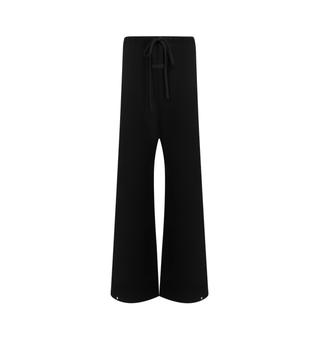 Image 1 of 3 - BLACK - FEAR OF GOD ESSENTIALS Bonded Canvas Work Pant crafted from a bonded stretch fabric featuring loose leg fit, side pockets, an encased elastic waistband with drawstrings, and metal snap hardware at the bottom hem. Additionally, a "Fear of God Essentials" rubberized label is stitched at the center front. 94% polyester, 6% spandex.