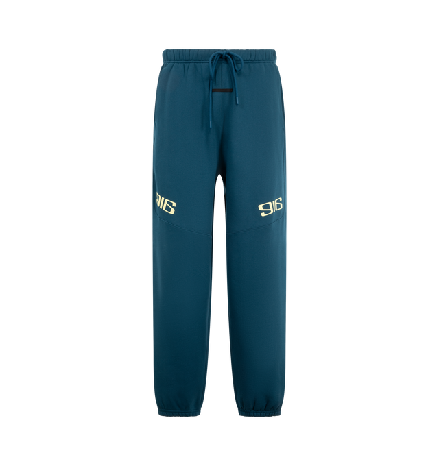 Image 1 of 3 - BLUE - Fear of God ESSENTIALS Classic Moto Sweatpant is crafted from heavyweight 380 GSM cotton-blend fleece and features a relaxed classic-fit silhouette with motocross-inspired seam detailing. Designed with signature 916 puff-print graphics at the front and FGX puff-print graphics extending down the back of the legs, this elevated sweatpant is finished with an encased elastic waistband, internal drawstring, elasticized cuffs, and side-seam pockets for everyday comfort and functionality. Mai