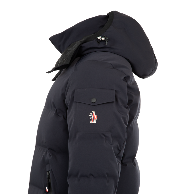 Image 4 of 4 - NAVY - MONCLER GRENOBLE Montgetech Down Jacket featuring a 2 way zip front closure, stand collar, removable hood, wrist gaiters, thumbhole cuffs, and an interior powder skirt. Lined with down fill. 87% polyamide/nylon, 13% elastane/spandex. Lining: 100% polyester. Padding: 90% down, 10% feather. Made in Romania.