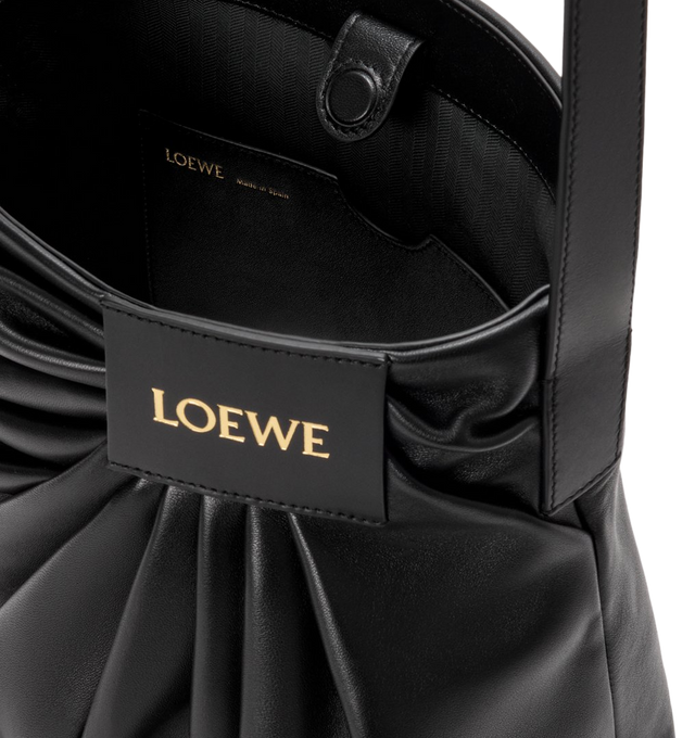 Image 4 of 4 - BLACK - LOEWE Draped Tote featuring soft scultpural shape and a wide strap adorned with a bold LOEWE-engraved buckle, shoulder or crossbody carry, adjustable strap, magnetic closure, one internal calfskin patch pocket, herringbone cotton canvas lining and gold embossed LOEWE. Mellow nappa lambskin. 30 cm x 29 cm x 13 cm. Made in Spain. This item may be restricted for online purchase to international clients. For assistance purchasing this item please contact our dedicated stylist team at pers