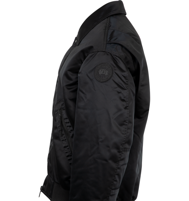 Image 3 of 3 - BLACK - CANADA GOOSE Seguin Aviator Bomber featuring double placket with coin-snap closure, dropped shoulders, rib-knit cuffs and hem, interior backpack straps for hands-free carrying capabilities, two fleece-lined zippered hand pockets, one sleeve pocket, one pen pocket with snap closure and ribbed waist. 100 % recycled polyamide. Made in Canada.