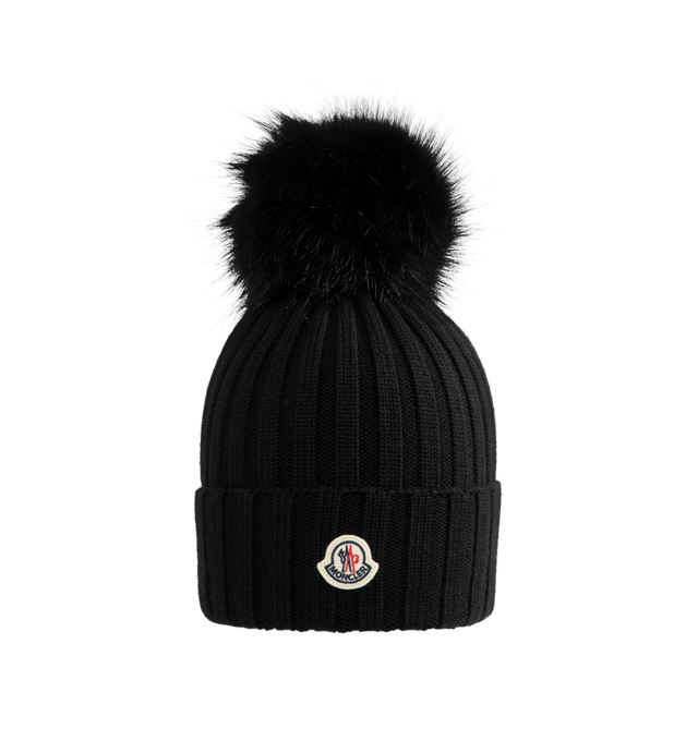 Image 1 of 2 - BLACK - Moncler Wool Beanie with Pom Pom features an English rib-knitting and logo at front and embellished with a faux fur pom pom. Designed to provide warmth, this heavy knit beanie for women adds the finishing touch to cold-weather looks. 100% virgin wool .
