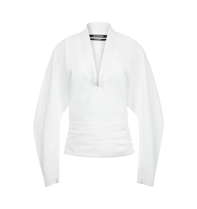 Image 1 of 2 - WHITE - Jacquemus Women's Draped Top is crafted from cotton poplin and features a fitted silhouette with draped detailing at the waist, a V-neckline, and long batwing sleeves with fitted cuffs. Finished with invisible zip closures at the cuffs and a side zip closure, this structured design balances volume and shape. Main Material: 100% Cotton. Made in Romania.