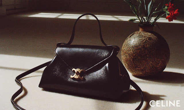 A black leather Celine handbag with a gold interlocking CC logo clasp, styled on a sunlit floor next to a decorative vase with red flowers. The Celine brand name is visible in the bottom right corner.