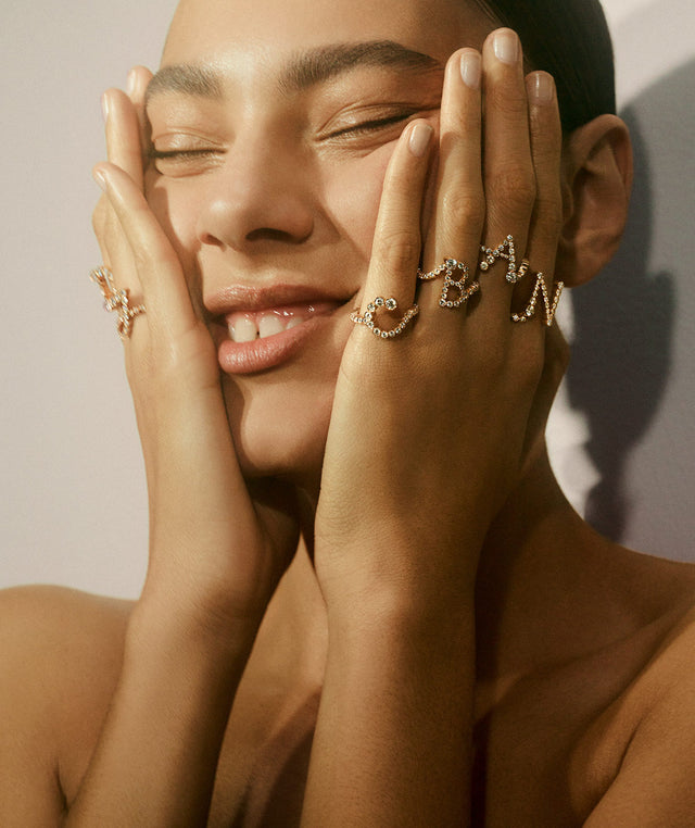 Woman wearing "C", "B", "A", "N" letter rings with diamonds by Sophie Bille Brahe 