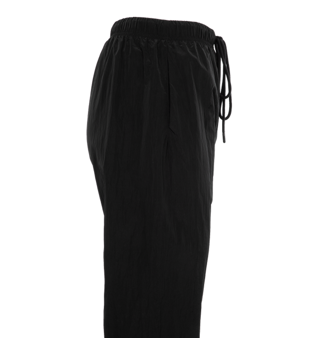 Image 3 of 4 - BLACK - FEAR OF GOD ESSENTIALS Crinkle Nylon Trackpants featuring an encased elastic waistband with elongated drawstrings, side seam pockets, an elastic hem with zipper adjustability at the ankle and a rubberized label at the center front. 100% nylon.  