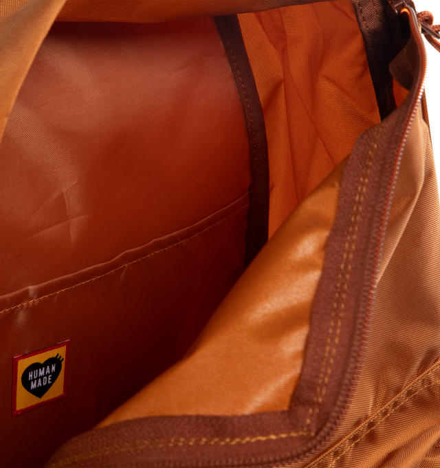 Image 3 of 3 - BROWN - HUMAN MADE Daypack featuring lightweight nylon Oxford exterior, PVC heart logo on the front, two-way zip closure, logo printed on top handle, front zip pocket, shoulder strap features a leather brand logo panel and one interior laptop sleeve. Capacity: around 20 L. 39cm x 34cm x 17cm.