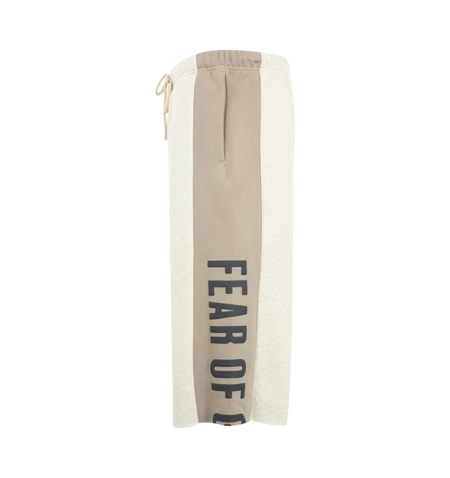 Image 3 of 4 - NEUTRAL - Fear of God Essentials Mens Sweatpants are crafted from heavyweight 380 GSM cotton-blend core fleece. Feature a wide-leg fit, paneled construction, elasticized waistband with bungee drawcord, side-seam pockets, raw-cut hem, puff-printed Fear of God and Essentials branding, and an Essentials logo label. Main Material: 80% Cotton, 20% Polyester.