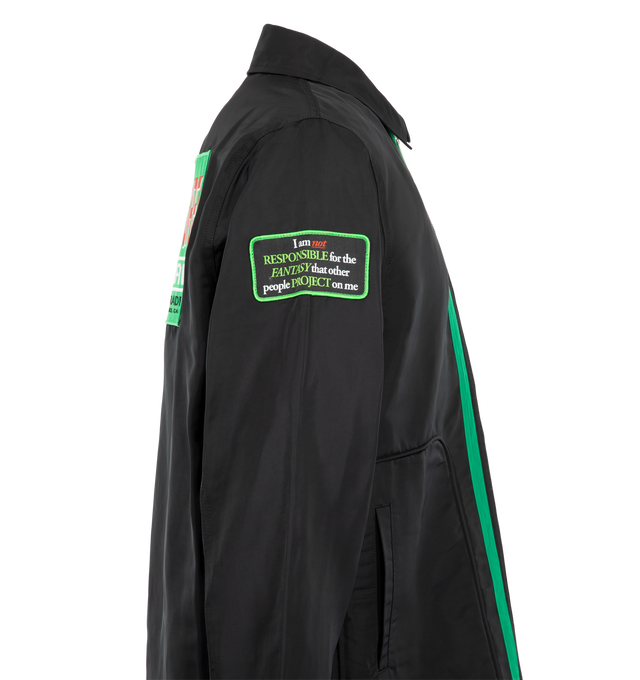Image 4 of 4 - BLACK - Pleasures Men's Records Jacket is designed with a structured silhouette and features a point collar, full two-way zip closure, and multiple embroidered and appliqu graphic patches throughout. A contrasting striped panel in green and white runs alongside the front zipper, while welt pockets and adjustable button tabs at the hem complete the design. Main material: Polyester.