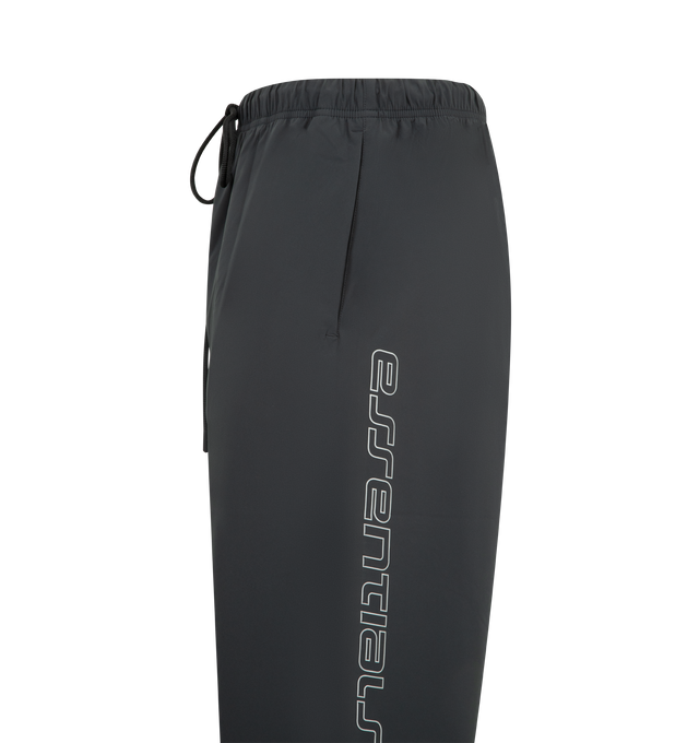 Image 3 of 3 - BLACK - FEAR OF GOD ESSENTIALS Tech Nylon Relaxed Track Pant featuring a tech nylon-spandex blend, pintuck relaxed-leg silhouette, metallic 3M-printed Essentials logo on leg, encased elastic waistband with elongated drawcords, side seam pockets and a Fear of God Essentials rubberized label stitched at the center front. 16% spandex, 84% nylon.