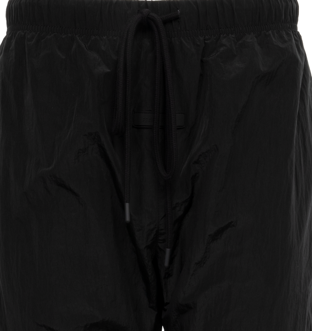 Image 4 of 4 - BLACK - FEAR OF GOD ESSENTIALS Crinkle Nylon Trackpants featuring an encased elastic waistband with elongated drawstrings, side seam pockets, an elastic hem with zipper adjustability at the ankle and a rubberized label at the center front. 100% nylon.  
