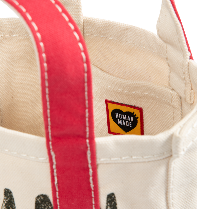 Image 3 of 3 - WHITE - HUMAN MADE Small Canvas Tote Bag featuring fleece-tough cotton canvas, wash finish creating a textured wrinkled look, seeped-in graphic, contrasting color accents on the handles and bottom, heart-shaped rivets on the side seams and external pocket attached to the side with the heart logo. 100% cotton.