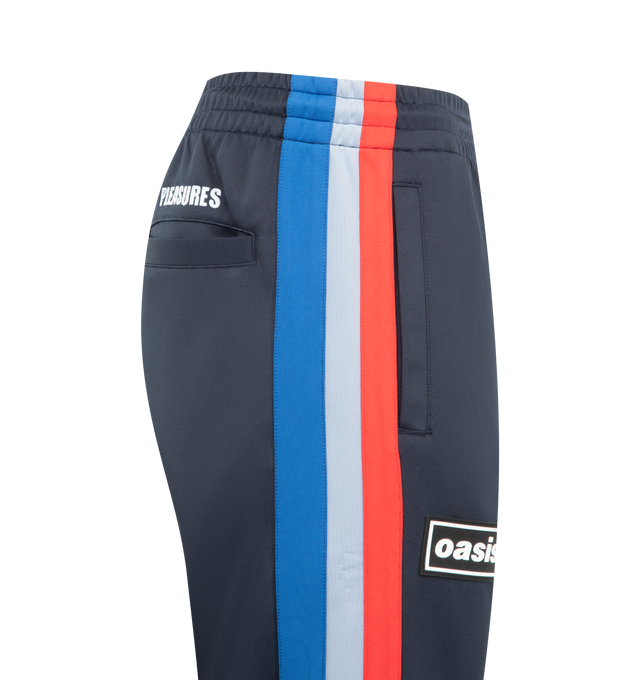 Image 3 of 3 - NAVY - PLEASURES Forever Track Pants featuring drawstring waistband, 3-pocket styling, rubberized front logo, straight leg and midweight pique fabric. 94% polyester, 6% spandex.