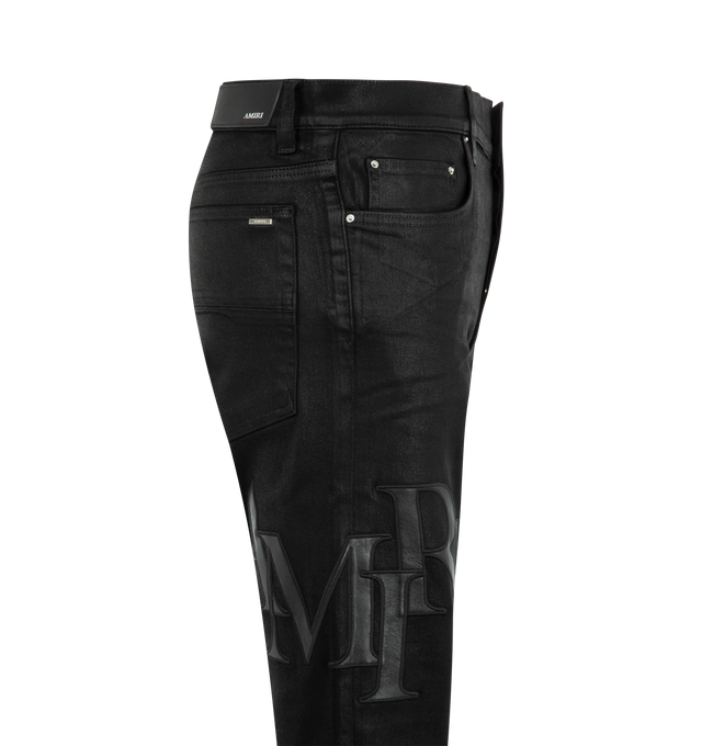 Image 3 of 3 - BLACK - AMIRI Staggered Logo Waxed Skinny Jeans featuring waxed stretch cotton denim, stacked Amiri logo on the left thigh, classic five-pocket styling and button zip closure. Cotton/polyester/elastane. Made in USA.