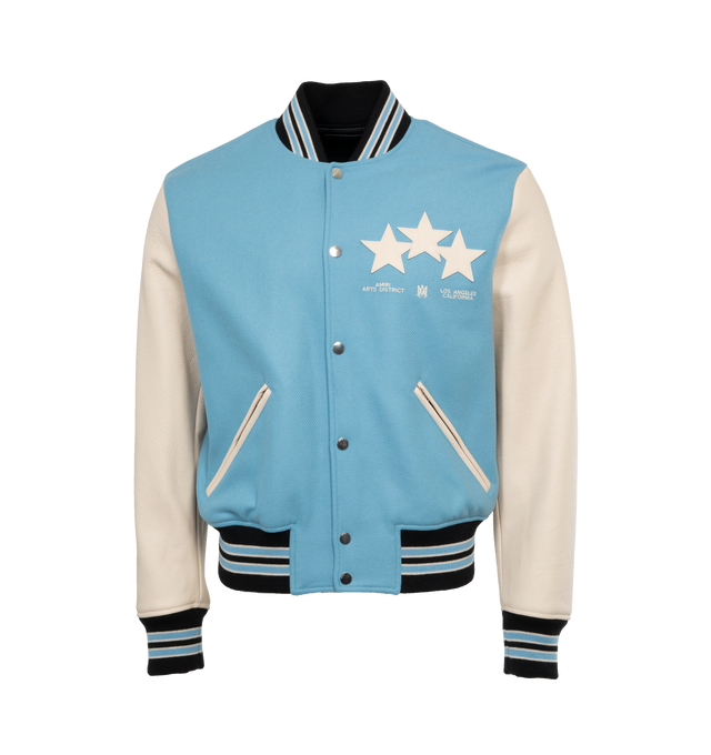 Image 1 of 4 - BLUE - AMIRI OVERSIZED STARS VARSITY JACKET crafted from durable light blue wool with leather contrast sleeves, adorned with a contellation of leather star appliques. Features contrast banded rib detailing at the waist, writsts and neck, welt zipper pockets, and classic snap button closure.  Wool shell, leather sleeves, viscose lining. Made in Italy.  