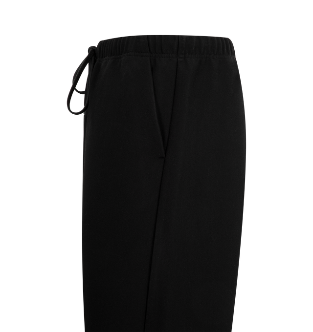 Image 3 of 3 - BLACK - FEAR OF GOD ESSENTIALS Bonded Canvas Work Pant crafted from a bonded stretch fabric featuring loose leg fit, side pockets, an encased elastic waistband with drawstrings, and metal snap hardware at the bottom hem. Additionally, a "Fear of God Essentials" rubberized label is stitched at the center front. 94% polyester, 6% spandex.