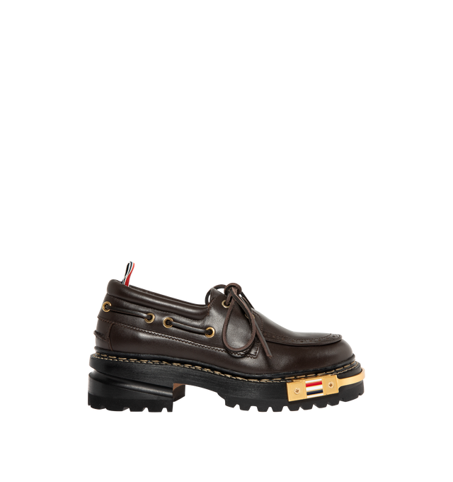 Image 1 of 4 - BROWN - THOM BROWNE Vitello Lug Boat Shoes featuring grained calfskin boat shoes, bumper hardware at toe with enameled stripes, perforated detailing at moc toe, lace-up closure, padded collar, serrated edge at sides and heel counter, tricolor grosgrain pull-loop at heel collar, buffed calfskin lining, stacked leather midsole and heel and treaded rubber sole. Heel: H2". Calfskin. Sole: rubber. Made in Italy.