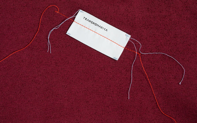 Burgundy fleece with white TRANSNOMADICA tag stitched on with multi-color thread