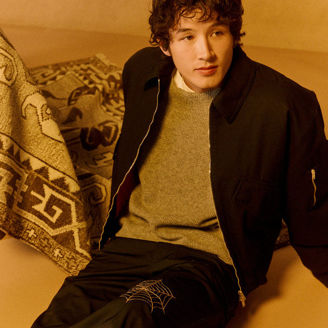 Man wearing Second layer black jacket over grey sweater with spiderweb detail pants 