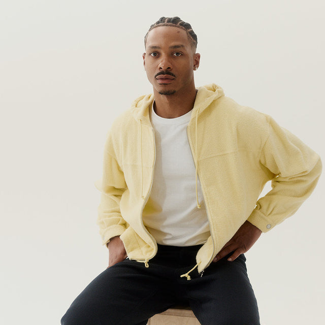 Man wearing Auralee pale yellow hooded sweatshirt over white teeshirt 