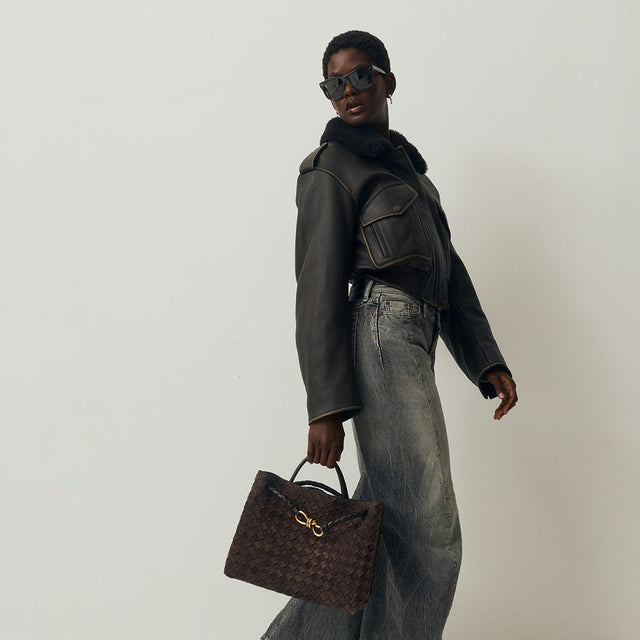 Woman wearing Acne Studios bomber jacket and jeans holding Bottega Veneta bag 