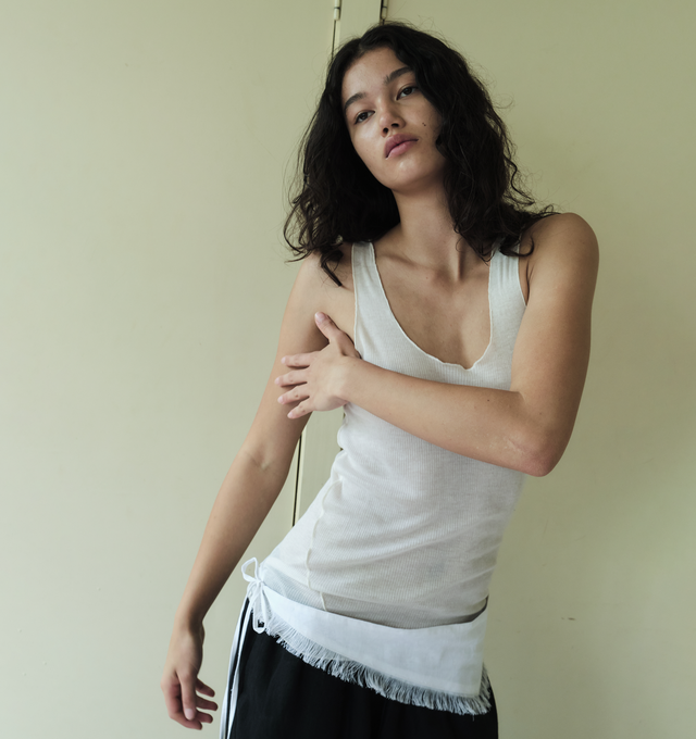 Image 3 of 3 - WHITE - DEIJI STUDIOS Knit Tank featuring a sheer fine knit tank with a low curved neckline and racer style back in a form fit, an asymmetric baby lock exposed hem detail and finishes. 65% ecovero viscose and 35% recycled polyester with OEKO-TEX 100 certification. 