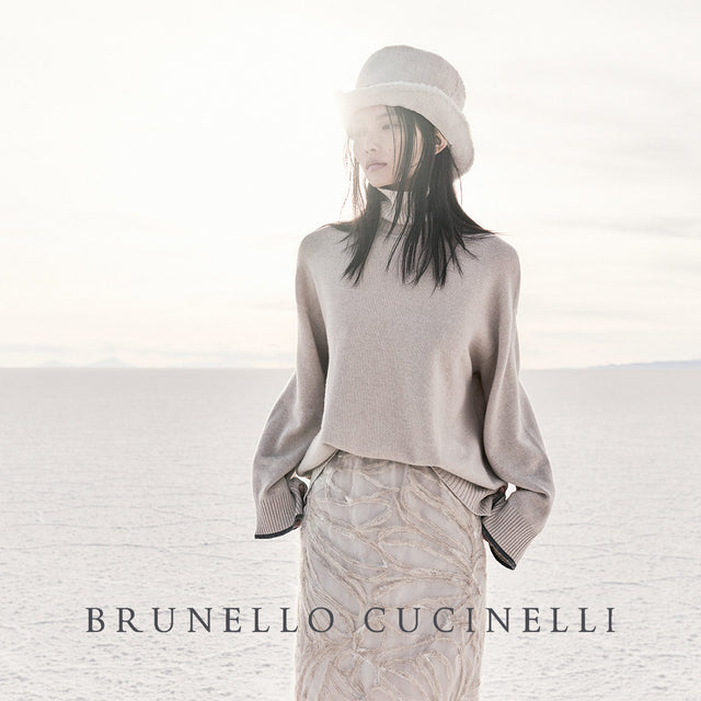 BRUNELLO CUCINELLI campaign featuring woman in beige sweater, skirt and bucket hat. Available in-store only at HIRSHLEIFERS.