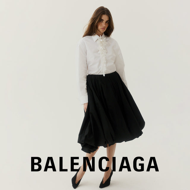 Woman wearing a white shirt and black skirt with 'BALENCIAGA' branding on a plain background 