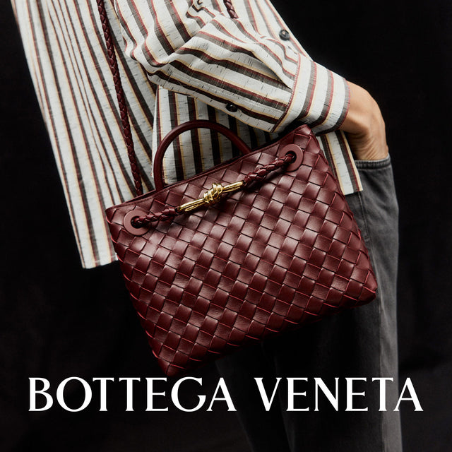 Person holding a woven brown handbag with Bottega Veneta branding. 