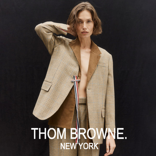 Model wearing a beige Thom Browne suit against a black background 