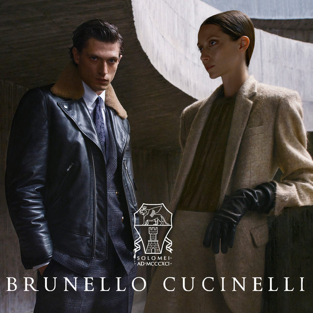 Man in black leather jacket with shearling collar and woman dressed in beige wool jacket and skirt, all from Brunello Cucinelli Fall 2024 collection  