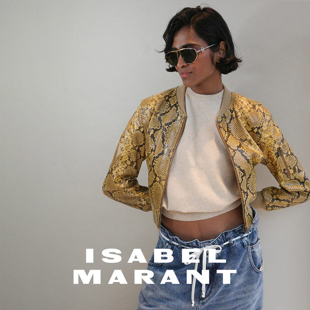 Woman wearing yellow and black snake pattern leather cropped jacket and blue denim jeans with white string belt, both by designer Isabel Marant